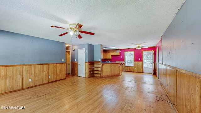 unfurnished living room with light hardwood / wood-style floors, a textured ceiling, wooden walls, and ceiling fan