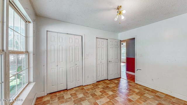 unfurnished bedroom featuring a textured ceiling and multiple closets