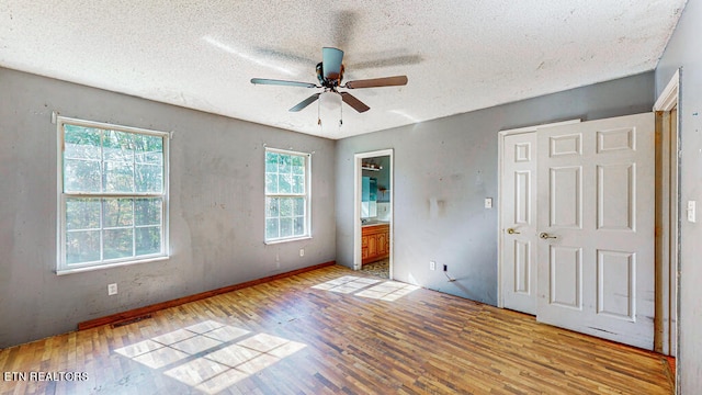 unfurnished bedroom featuring a textured ceiling, connected bathroom, light wood-type flooring, and ceiling fan