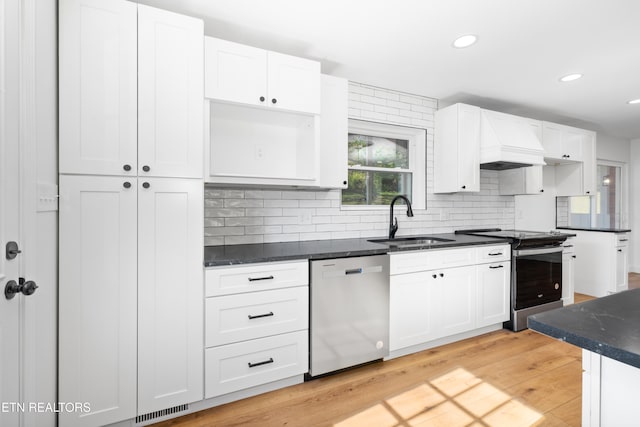 kitchen featuring appliances with stainless steel finishes, premium range hood, sink, and light wood-type flooring