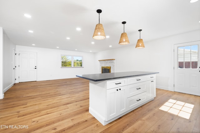 kitchen with white cabinetry, hanging light fixtures, light wood-type flooring, and a brick fireplace