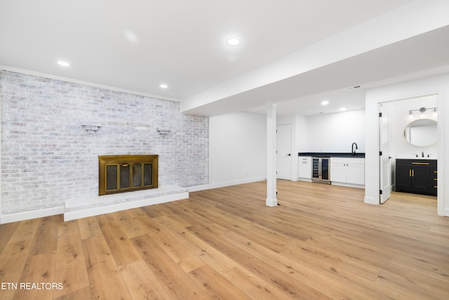 unfurnished living room with light hardwood / wood-style floors, brick wall, a brick fireplace, and beverage cooler