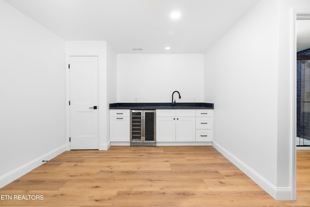 bar with wine cooler, sink, white cabinetry, and light hardwood / wood-style floors