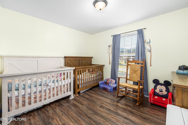 bedroom featuring a nursery area and dark hardwood / wood-style flooring