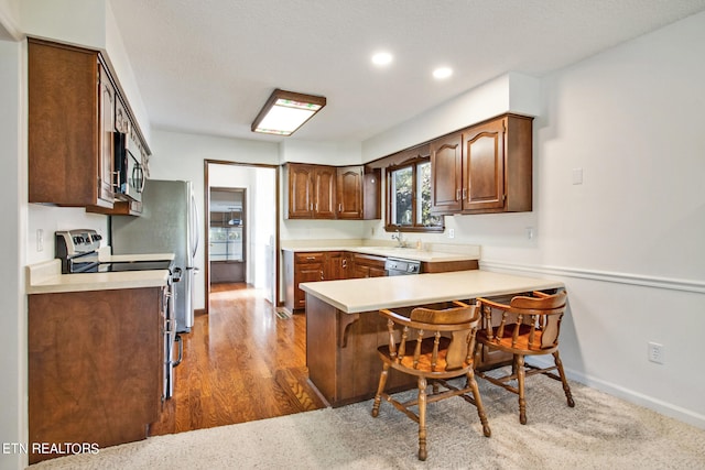 kitchen with kitchen peninsula, stainless steel appliances, sink, hardwood / wood-style floors, and a kitchen bar