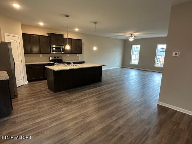 kitchen with ceiling fan, a center island with sink, appliances with stainless steel finishes, and baseboards