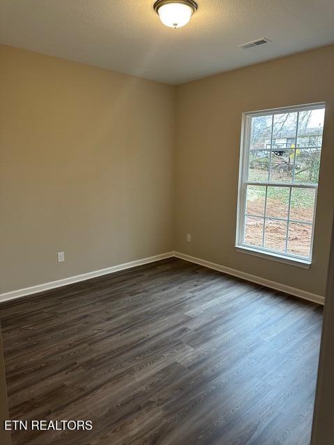 empty room with a textured ceiling, dark wood finished floors, visible vents, and baseboards