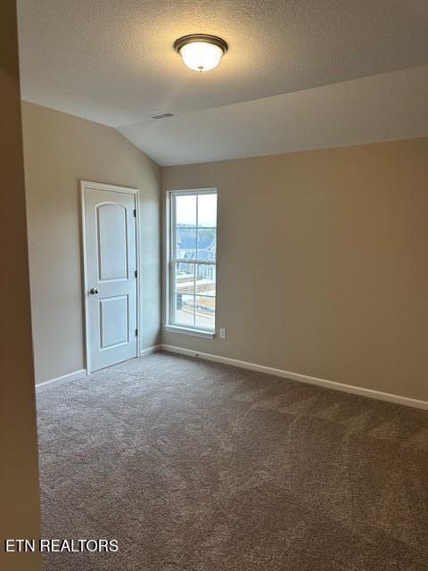 empty room with lofted ceiling, dark colored carpet, visible vents, a textured ceiling, and baseboards