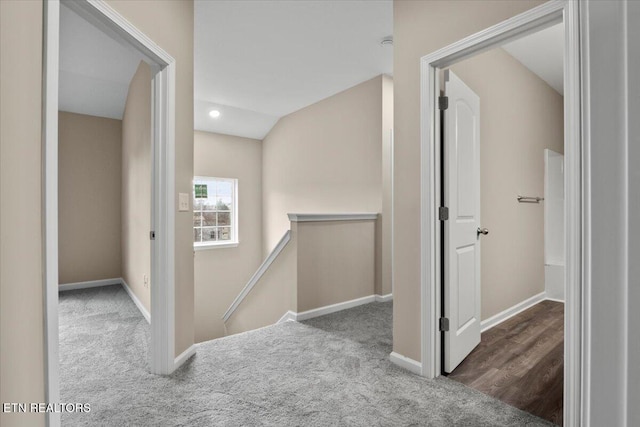 hallway with carpet, baseboards, vaulted ceiling, and an upstairs landing