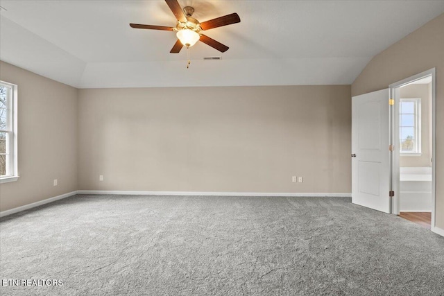 carpeted empty room featuring lofted ceiling, ceiling fan, visible vents, and baseboards