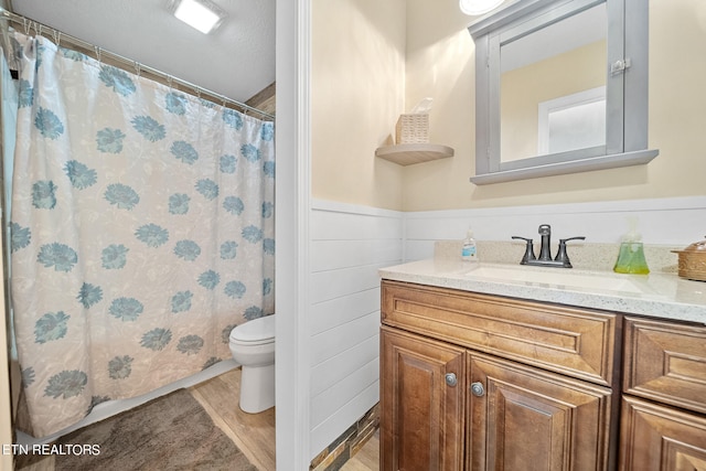 bathroom with a wainscoted wall, curtained shower, toilet, vanity, and wood finished floors