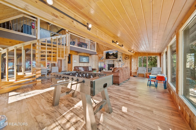 playroom featuring light hardwood / wood-style flooring, a stone fireplace, wooden ceiling, and wood walls