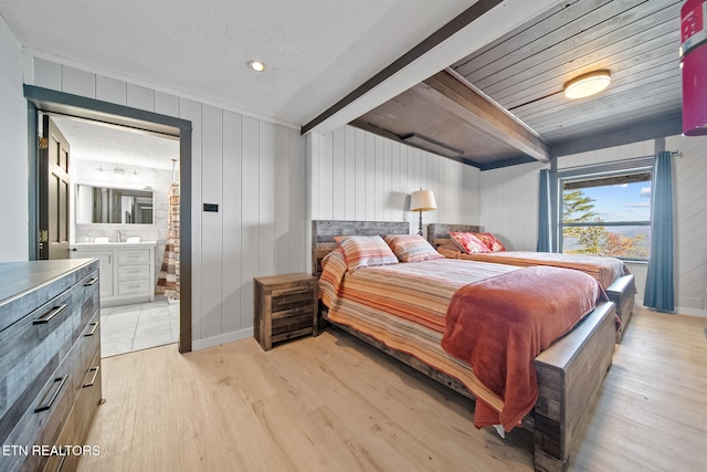 bedroom with light hardwood / wood-style floors, wood walls, beamed ceiling, and connected bathroom