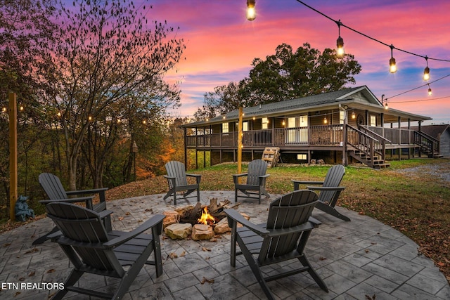 patio terrace at dusk featuring a fire pit, a wooden deck, and a lawn