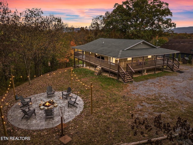 back house at dusk featuring a wooden deck, a patio, and an outdoor fire pit