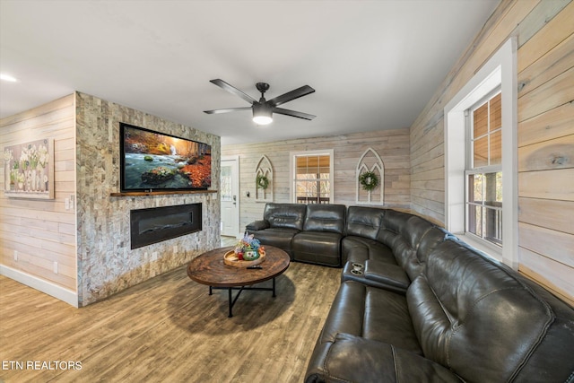 living room with a stone fireplace, wood walls, hardwood / wood-style flooring, and ceiling fan