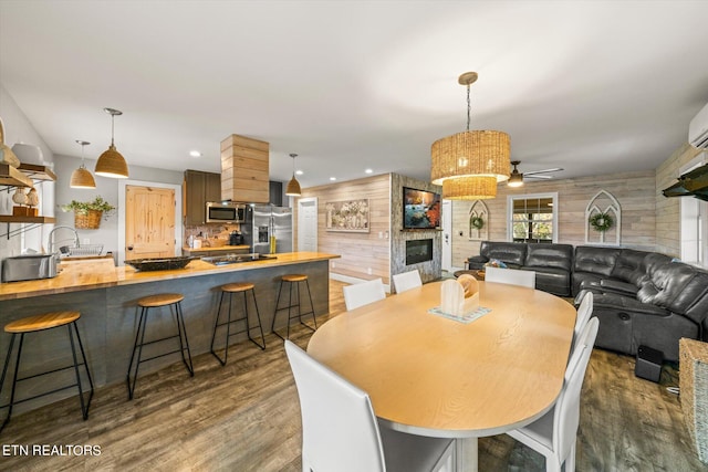 dining room with a large fireplace, wood walls, dark hardwood / wood-style floors, and ceiling fan