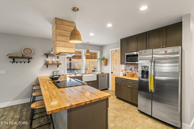 kitchen with butcher block countertops, kitchen peninsula, stainless steel appliances, decorative light fixtures, and a breakfast bar area