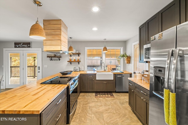 kitchen with sink, butcher block countertops, hanging light fixtures, and stainless steel appliances