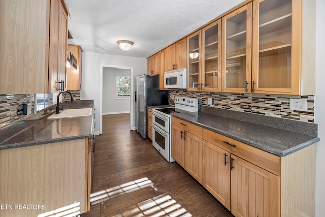 kitchen featuring white appliances, a sink, dark wood-style floors, tasteful backsplash, and dark countertops