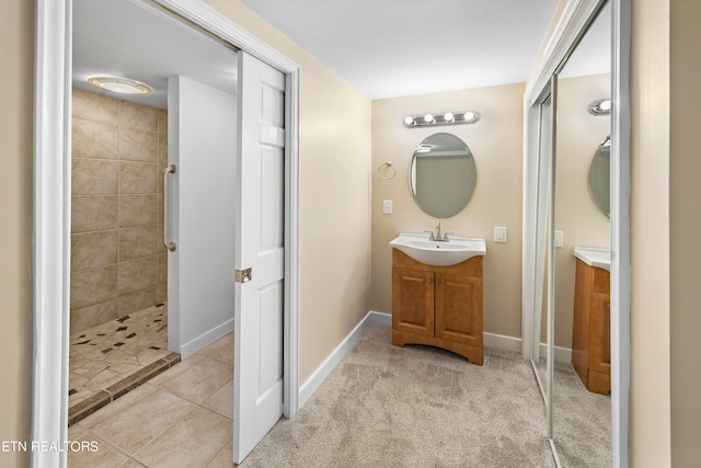 full bath with tile patterned flooring, a tile shower, vanity, and baseboards