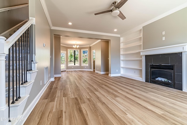 unfurnished living room featuring light hardwood / wood-style floors, a tile fireplace, crown molding, built in features, and ceiling fan with notable chandelier