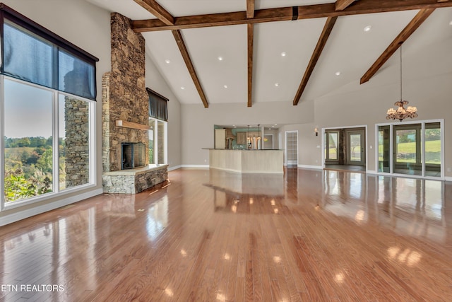 unfurnished living room with a stone fireplace, beam ceiling, an inviting chandelier, high vaulted ceiling, and light hardwood / wood-style floors