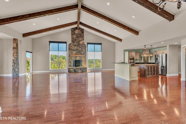 unfurnished living room featuring beam ceiling, a stone fireplace, high vaulted ceiling, and light hardwood / wood-style floors