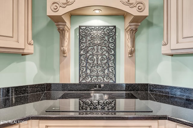 interior space featuring black electric stovetop, ornate columns, cream cabinets, and dark stone counters