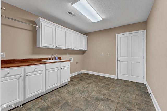 washroom featuring electric dryer hookup, washer hookup, sink, cabinets, and a textured ceiling