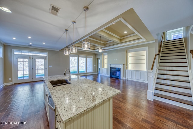 kitchen with a kitchen island with sink, dark hardwood / wood-style floors, hanging light fixtures, sink, and light stone counters