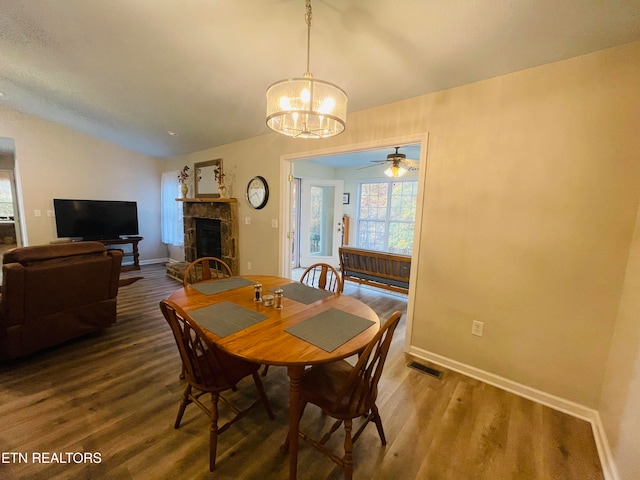 dining area featuring wood-type flooring, vaulted ceiling, ceiling fan with notable chandelier, and a stone fireplace