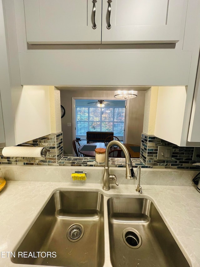 kitchen featuring ceiling fan, backsplash, white cabinets, light stone counters, and sink