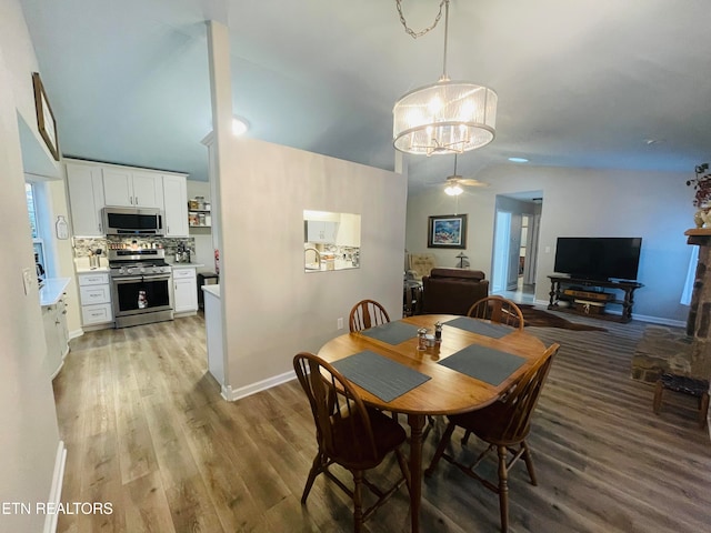 dining space featuring vaulted ceiling, ceiling fan with notable chandelier, and light hardwood / wood-style flooring