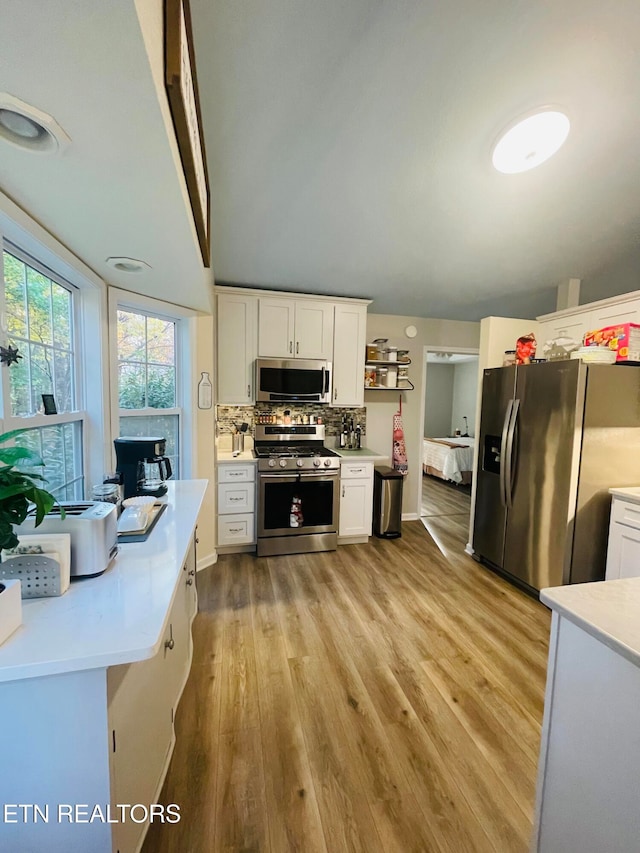 kitchen with light wood-type flooring, appliances with stainless steel finishes, decorative backsplash, and white cabinetry