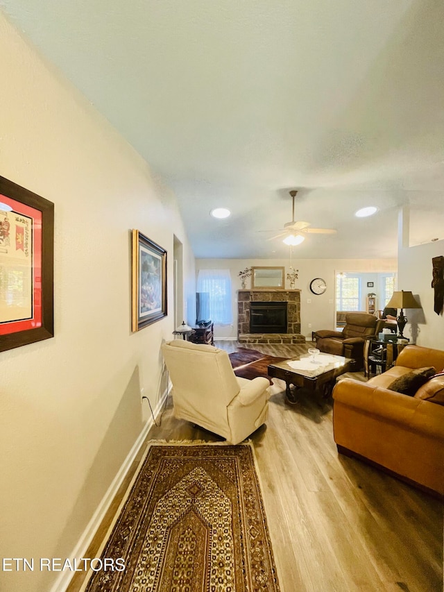 living room featuring ceiling fan, hardwood / wood-style flooring, and a stone fireplace