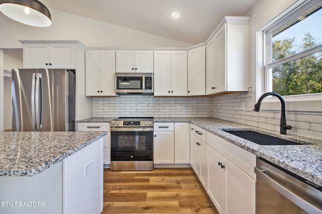 kitchen with lofted ceiling, tasteful backsplash, white cabinetry, sink, and stainless steel appliances