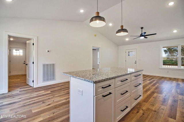 kitchen featuring hanging light fixtures, white cabinetry, hardwood / wood-style floors, vaulted ceiling, and light stone counters