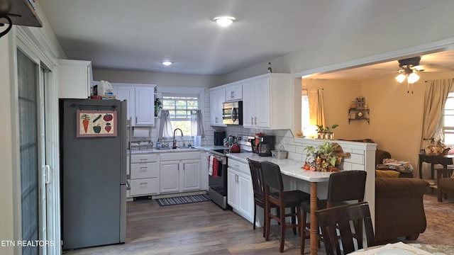 kitchen with sink, appliances with stainless steel finishes, white cabinetry, tasteful backsplash, and kitchen peninsula