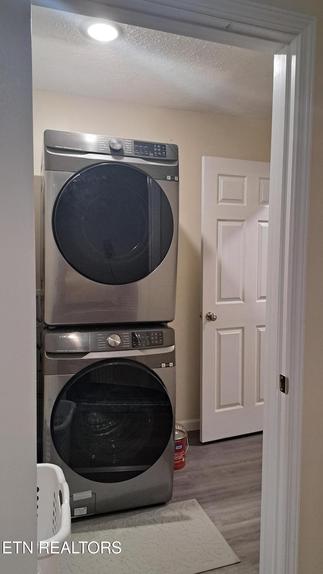 laundry room with stacked washer and clothes dryer, wood-type flooring, and a textured ceiling