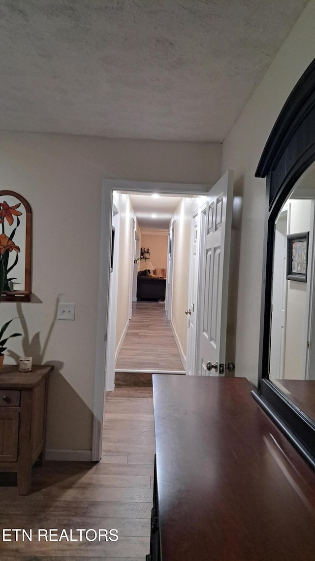 hallway with a textured ceiling and light hardwood / wood-style flooring