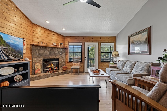 living room featuring a textured ceiling, vaulted ceiling, a stone fireplace, and wood-type flooring