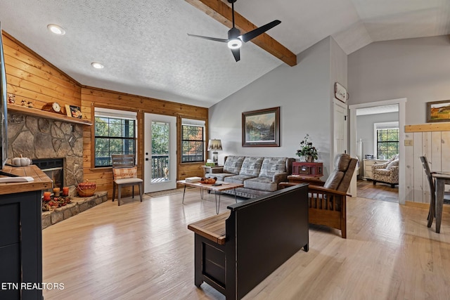 living room with ceiling fan, a textured ceiling, light wood-type flooring, a fireplace, and wooden walls