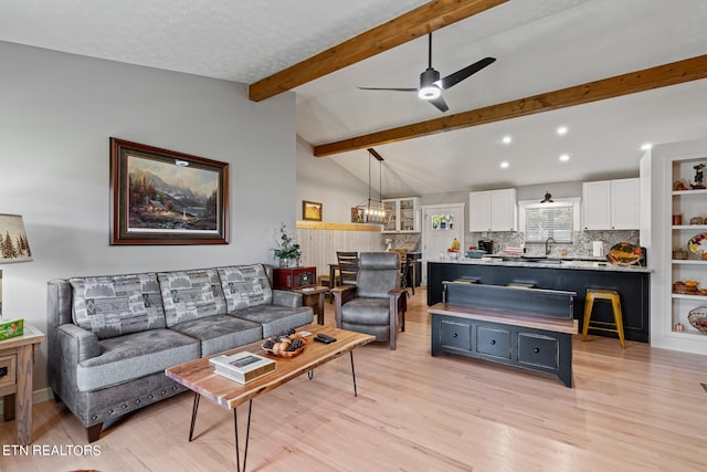 living room featuring a textured ceiling, light hardwood / wood-style flooring, vaulted ceiling with beams, and ceiling fan with notable chandelier