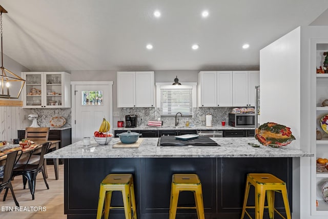 kitchen featuring light stone countertops, hanging light fixtures, stainless steel appliances, white cabinets, and a breakfast bar area