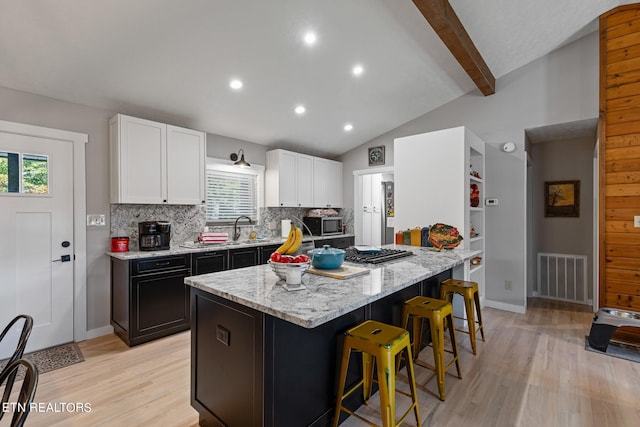 kitchen with vaulted ceiling with beams, light hardwood / wood-style flooring, white cabinets, and a wealth of natural light