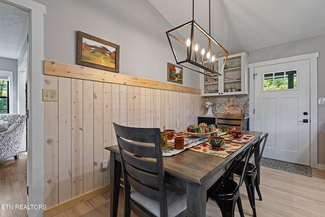 dining area with lofted ceiling, a chandelier, light wood-type flooring, and wooden walls