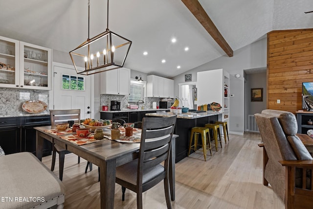 dining space featuring beamed ceiling, light hardwood / wood-style flooring, an inviting chandelier, high vaulted ceiling, and wood walls