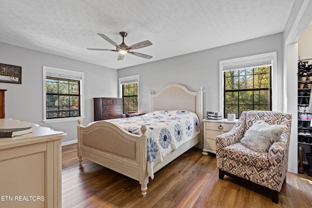 bedroom featuring multiple windows, a textured ceiling, dark wood-type flooring, and ceiling fan