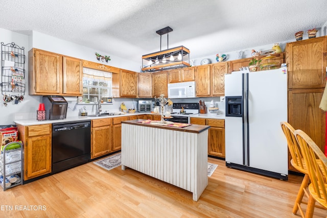 kitchen featuring white appliances, sink, light wood-type flooring, a textured ceiling, and pendant lighting